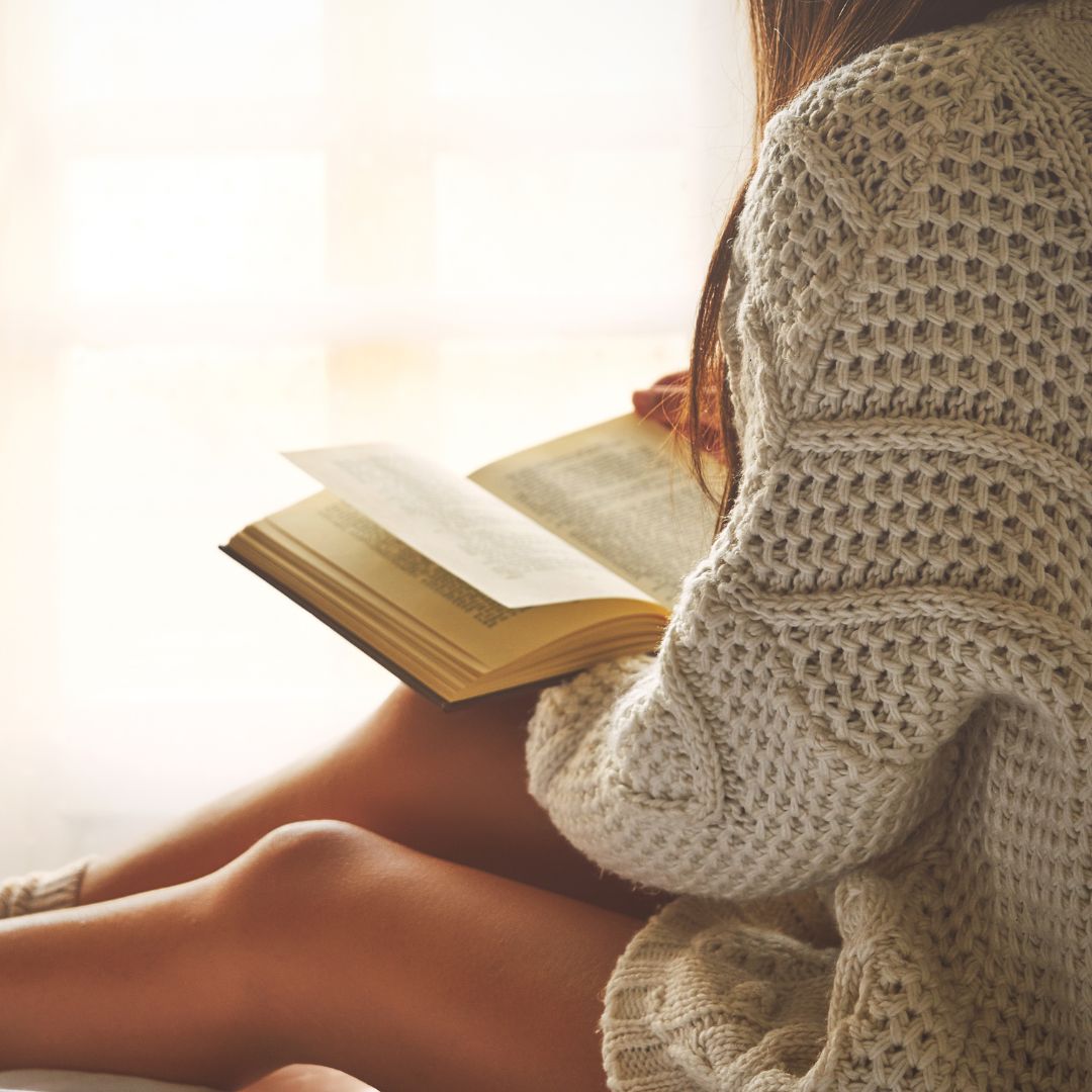 Woman in a cardigan reading a book by a window